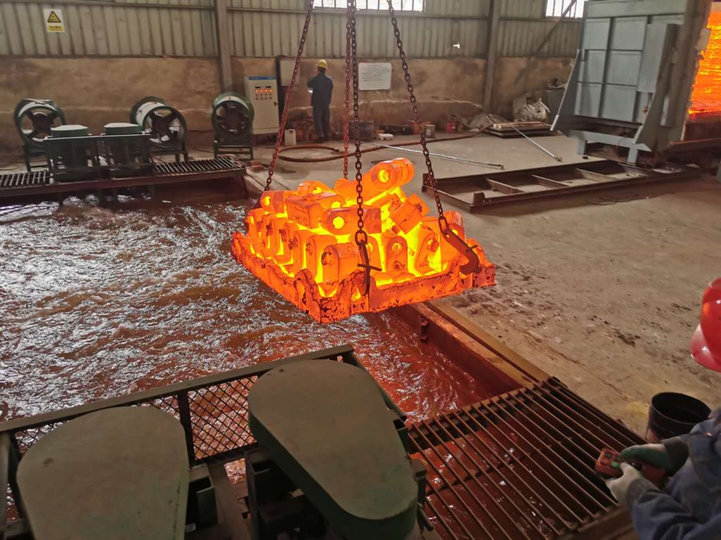 Bright orange-red hot crusher wear part castings lifted by chains after heat treatment quenching process at ZHILI manufacturing facility